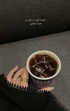 a woman holding a cup of coffee on top of a couch with her hand in the cup