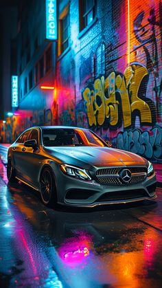 a car parked in front of a building with graffiti on the wall behind it at night