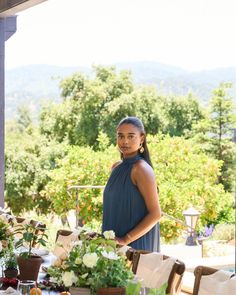 a woman standing in front of a table with flowers and fruit on top of it