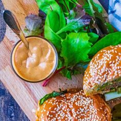 two hamburgers with lettuce, tomato and mayonnaise on a cutting board