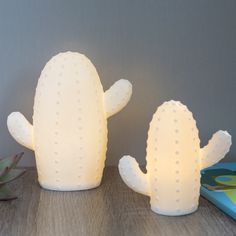 two white cactus shaped lights sitting on top of a wooden table next to a plant