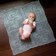 a baby drinking from a bottle on top of a blue rug in the middle of a wooden floor