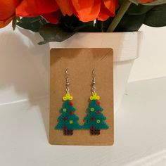 a pair of christmas tree earrings sitting on top of a piece of paper next to flowers