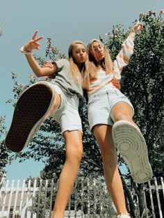 two young women standing next to each other in front of a white fence and trees