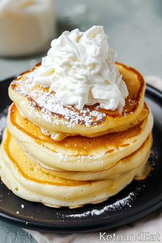 a stack of pancakes topped with whipped cream on a black plate next to a glass of milk