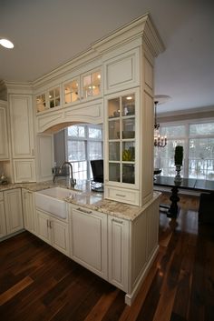 a large kitchen with white cabinets and wood flooring in front of a window that leads to an outside patio