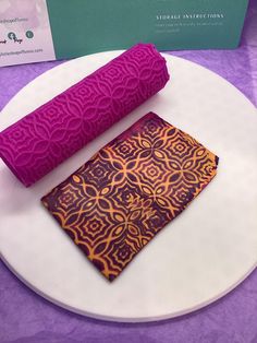 two pieces of fabric sitting on top of a white plate next to a purple napkin