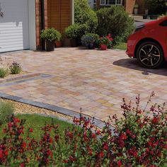 a red car parked in front of a house with flowers and shrubs around the driveway