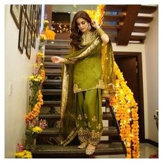 a woman standing on some stairs with flowers around her and wearing a green outfit that is draped over her shoulders