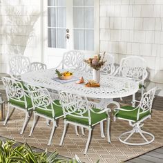 an outdoor dining table with green cushions and white chairs on a patio area next to a potted plant