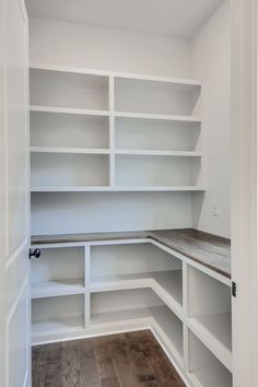 an empty walk in closet with white shelving and wood flooring on the side