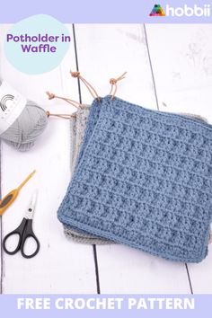 a crochet potholder in blue sits on a white table next to scissors and yarn