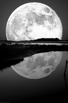 the full moon is reflected in water on a black and white night with reflection from it's surface