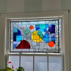 a stained glass window with geometric designs on the bottom and sides, above a potted plant