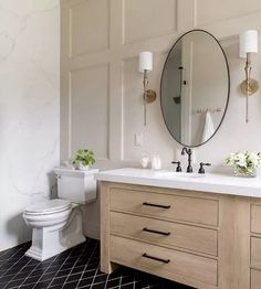 a white toilet sitting next to a bathroom sink under a mirror on top of a wooden cabinet