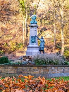 a statue in the middle of a park surrounded by trees and bushes with leaves around it