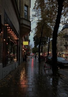 a rainy street with cars parked on the side and people walking down the sidewalk at night