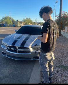 a young man standing in front of a silver sports car with black and white stripes