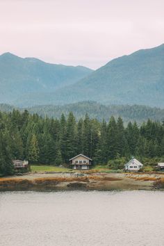 some houses are sitting on the shore of a lake with mountains in the background