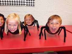 four children with their mouths open sitting in front of a red table topped with fake spider legs