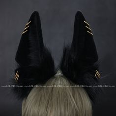 a wig with black feathers and gold pins on it's ears is shown in front of a dark background