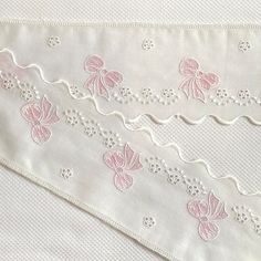 white and pink embroidered fabric with flowers on the side, along with lace trimming