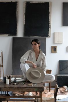 a woman sitting on top of a wooden table holding a white hat in her hands