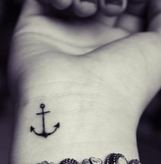 an anchor tattoo on someone's wrist is shown in black and white, with the word