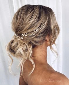 a woman with blonde hair wearing a gold headband and pearls in her hair is seen from the back