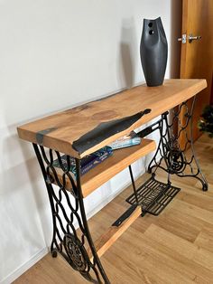 an old sewing machine table with a vase on top and books under the table next to it