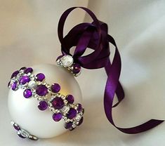 a white ornament with purple and clear jeweled decorations on it's side