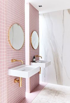 two sinks and mirrors in a bathroom with pink tiles on the walls, gold accents