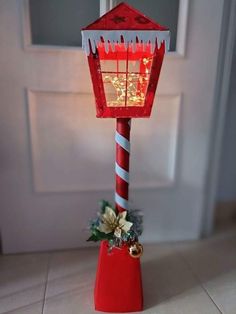 a red and white lamp on top of a table next to a door with flowers in it