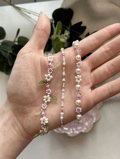 the hand is holding three bracelets with pearls and leaves