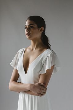 a woman in a white dress with her arms crossed and looking off to the side