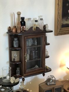 a cabinet with many bottles on top of it next to a lamp and pictures hanging on the wall