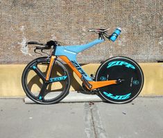 a blue and orange bike parked on the side of a road next to a brick wall