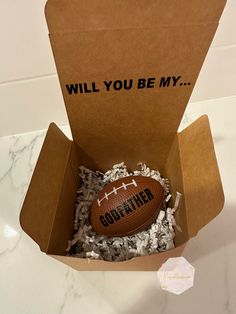 a football in a cardboard box with shredded paper around it that says, will you be my?