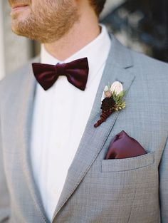 a man wearing a gray suit with a red bow tie and flower boutonniere