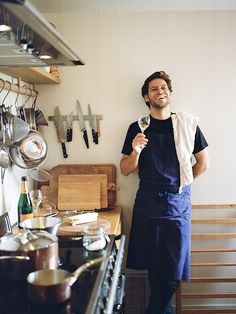 a man holding a wine glass standing in front of a kitchen counter with pots and pans hanging on the wall