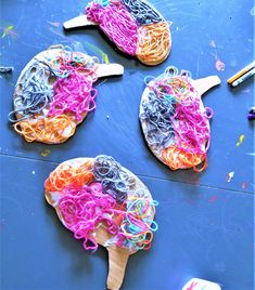 three wooden spoons filled with colored yarn and plastic noodles on top of a blue surface