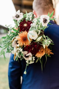 a man in a blue suit holding a bouquet of flowers and greenery on his back