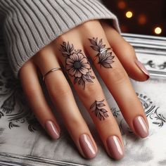 a woman's hand with three tattoos on her fingers and two flowers on the ring finger