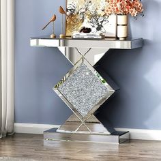 a silver table with a mirror and vase on it next to a window in a blue room