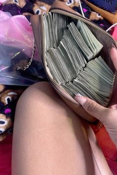 a woman is holding a purse full of money while sitting on the ground with her legs crossed