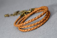 three braided leather bracelets with brass clasps on grey background, closeup