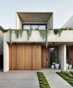 a modern house with wooden garage doors and green plants on the roof, along with brick walkway