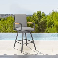 an outdoor bar stool next to a pool with trees and bushes in the back ground