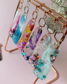 four different colored glass beads hanging from a gold holder on a pink surface with other items in the background