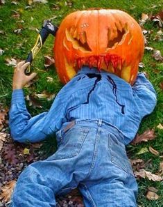 a person in overalls laying on the ground with an orange pumpkin over their head